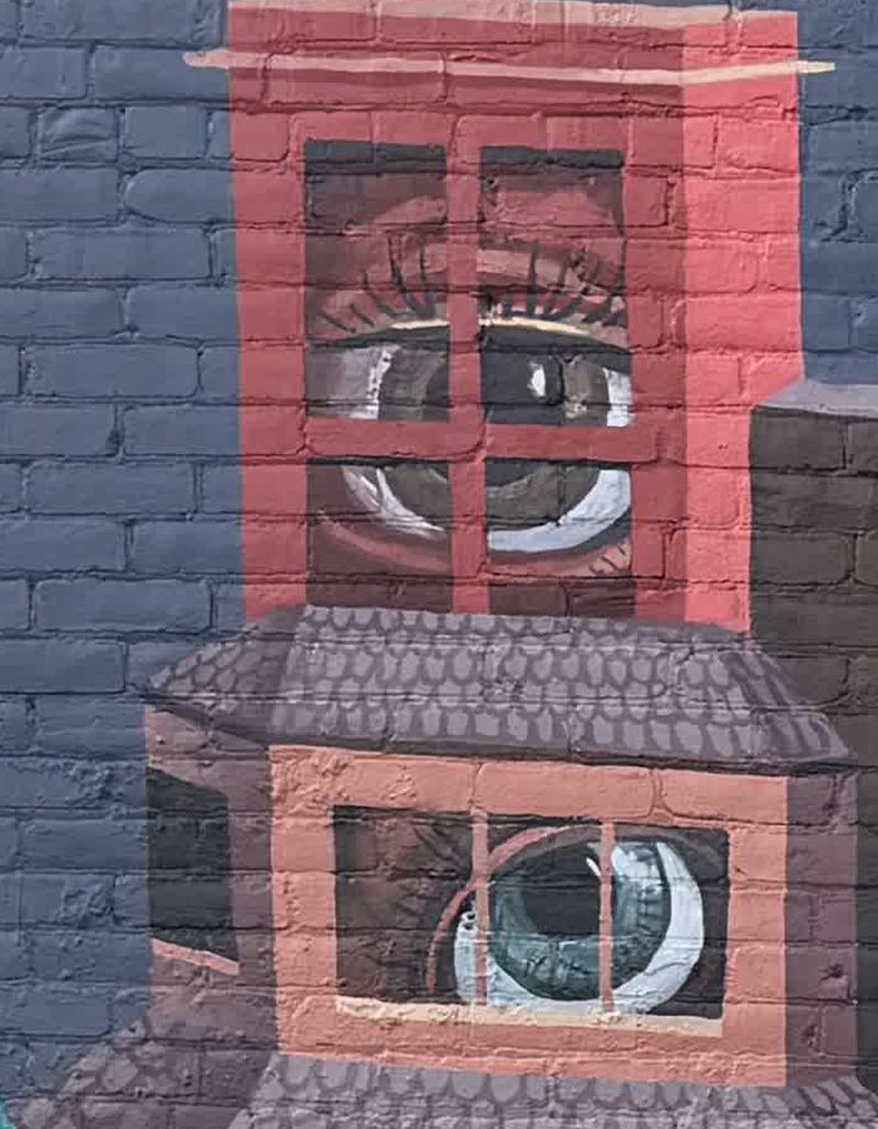 Two painted windows on a brick wall, each with a large painted eye looking out.